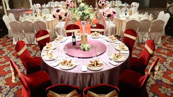 A round table with a purple tablecloth, surrounded by red chairs with gold sashes, set for a formal event.