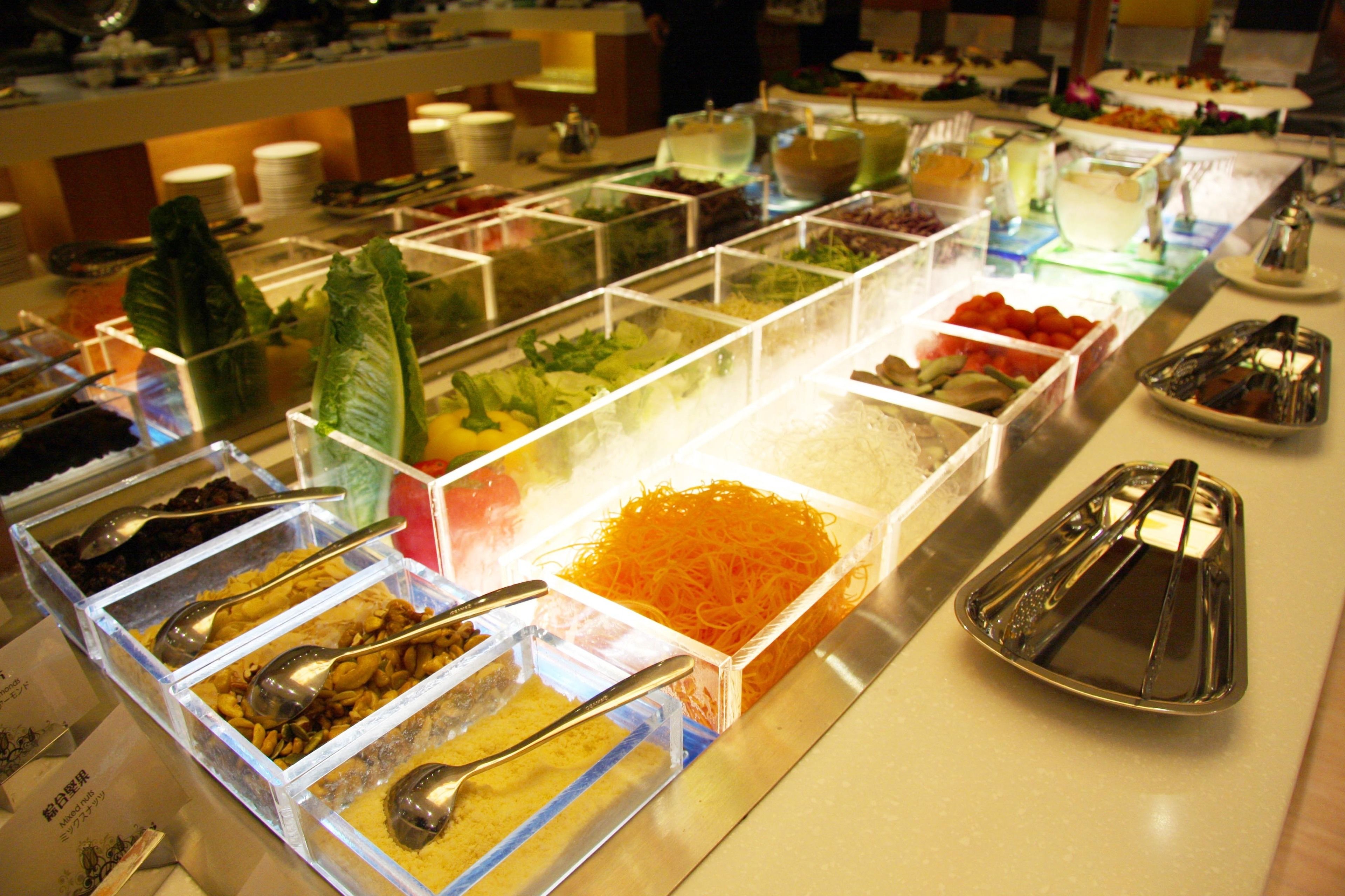 A buffet with various food items in clear containers, including salads, fruits, and grains.