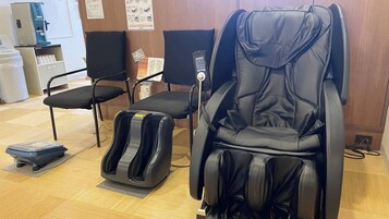 Una poltrona massaggiante, un massaggiatore per i piedi e un dispenser d'acqua in una stanza con pavimento di legno e sedie nere.