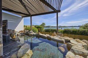 A stone pool with a wooden pergola, a staircase, and a view of a body of water and distant hills. - Hotel Harvest Nankitanabe (Tanabe)