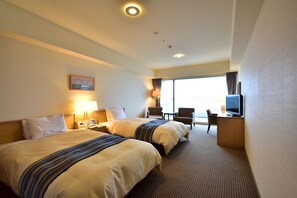 Ein Hotelzimmer mit zwei Betten, einem Schreibtisch mit Fernseher und einem Sessel.