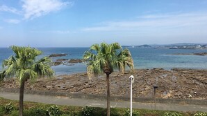 Vista costera con playa rocosa, palmeras y cielo despejado.