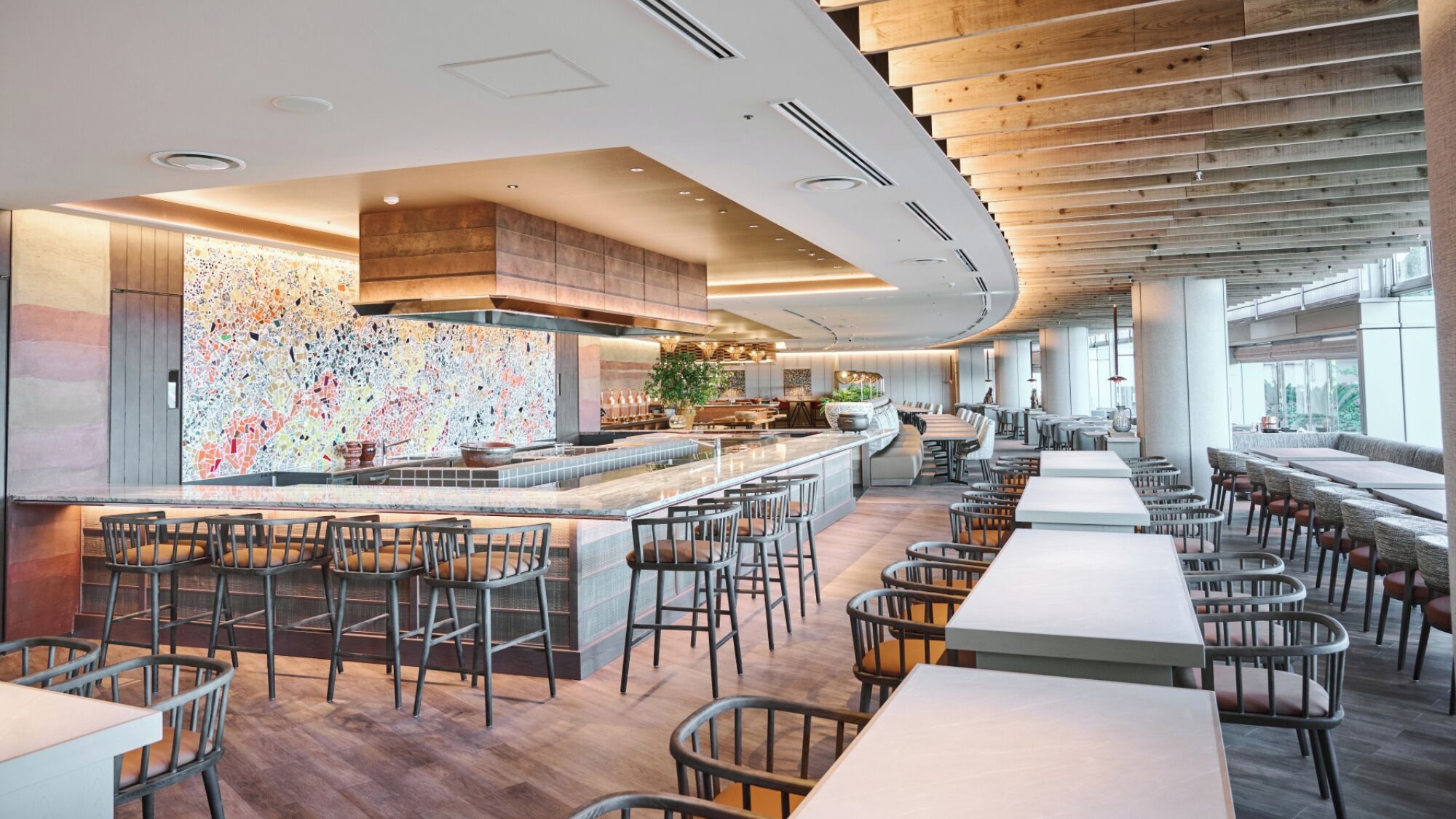 Een modern restaurant met een centrale bar, meerdere zitgedeeltes en een groot raam dat voor natuurlijk licht zorgt.