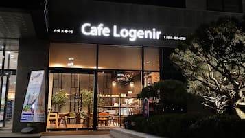 A Cafe Logenir storefront at night with illuminated signage, a glass entrance, and indoor seating visible through the windows.