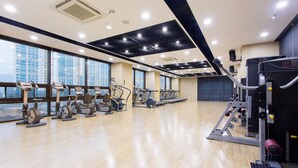 Une salle de sport équipée de machines de cardio, de matériel de musculation et de grandes fenêtres offrant une vue sur la ville.