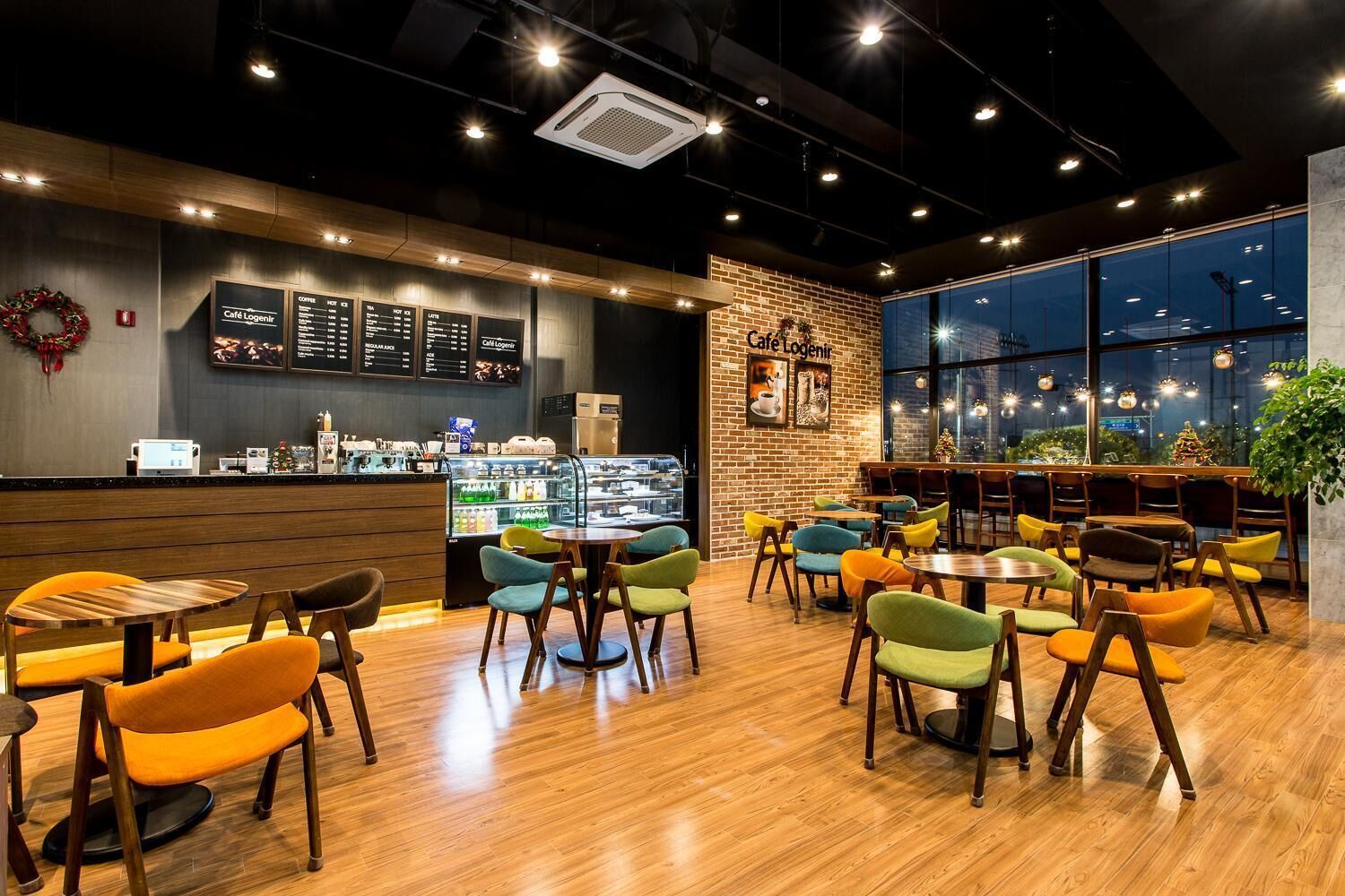 A café with wooden flooring, colorful chairs, a menu board, and a brick wall.
