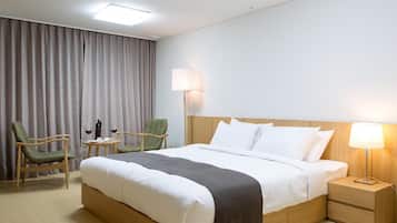 A hotel room with a large bed, two chairs, a bedside table with a lamp, and a window with curtains.