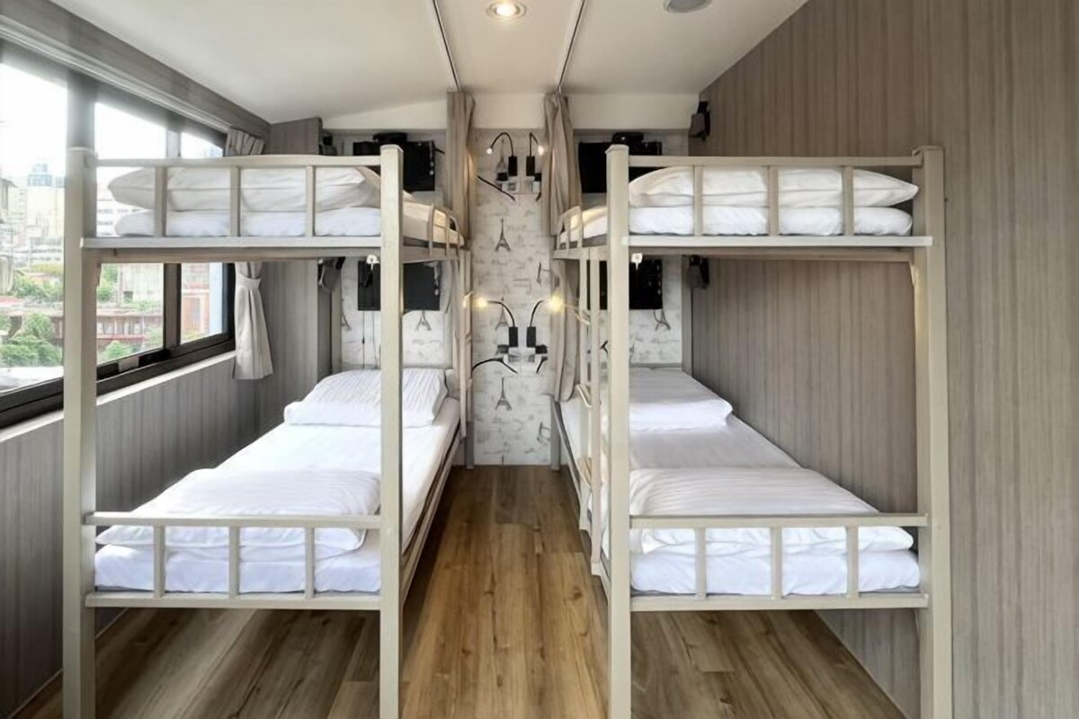 A bunk bed room with a wooden floor, a window with curtains, and a wall-mounted light fixture.