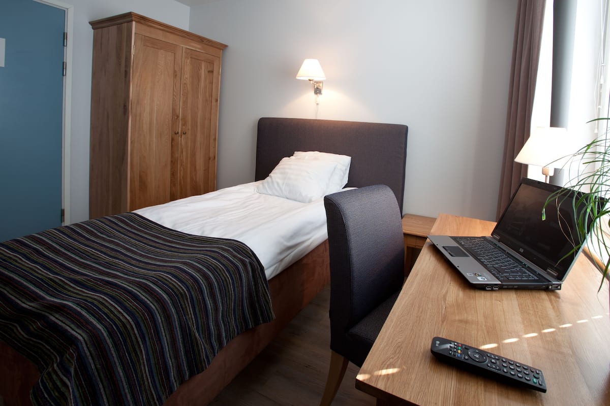 A hotel room with a bed, a desk with a laptop, a remote control, and a wardrobe.