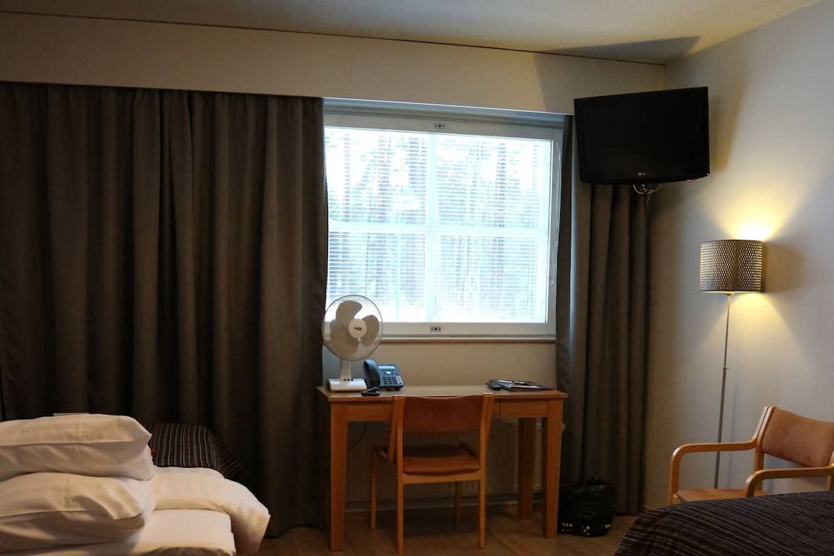 A hotel room with a bed, desk, chair, TV, and a window with curtains.