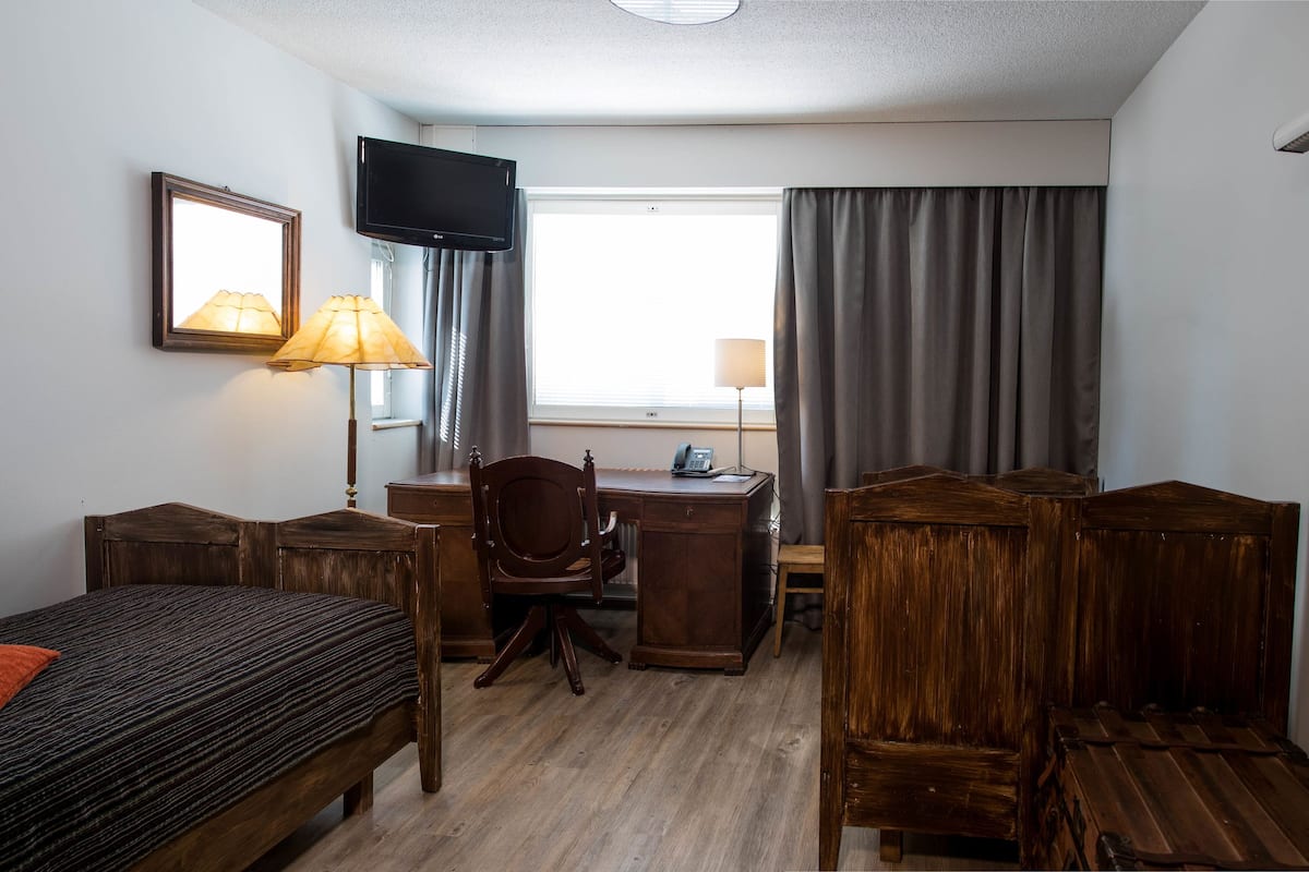 A hotel room with a bed, desk, chair, wardrobe, TV, and a window with curtains.