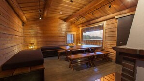 A cozy cabin interior with wooden walls, a dining table, benches, and a fireplace. - Majatalo Onnela (Tuusula)