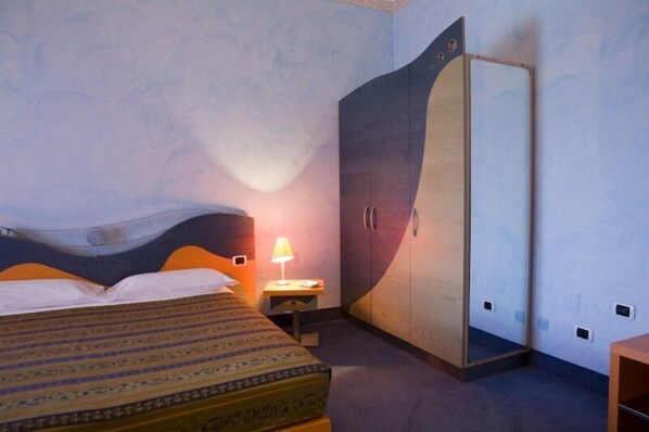 A hotel room with a bed, a nightstand with a lamp, and a wardrobe.