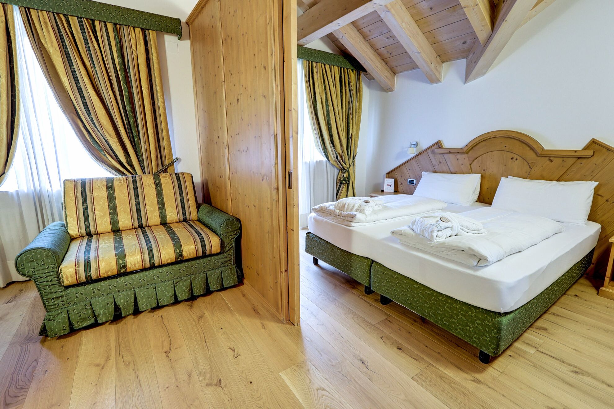 A room with a bed, a sofa, wooden flooring, and a wooden ceiling.