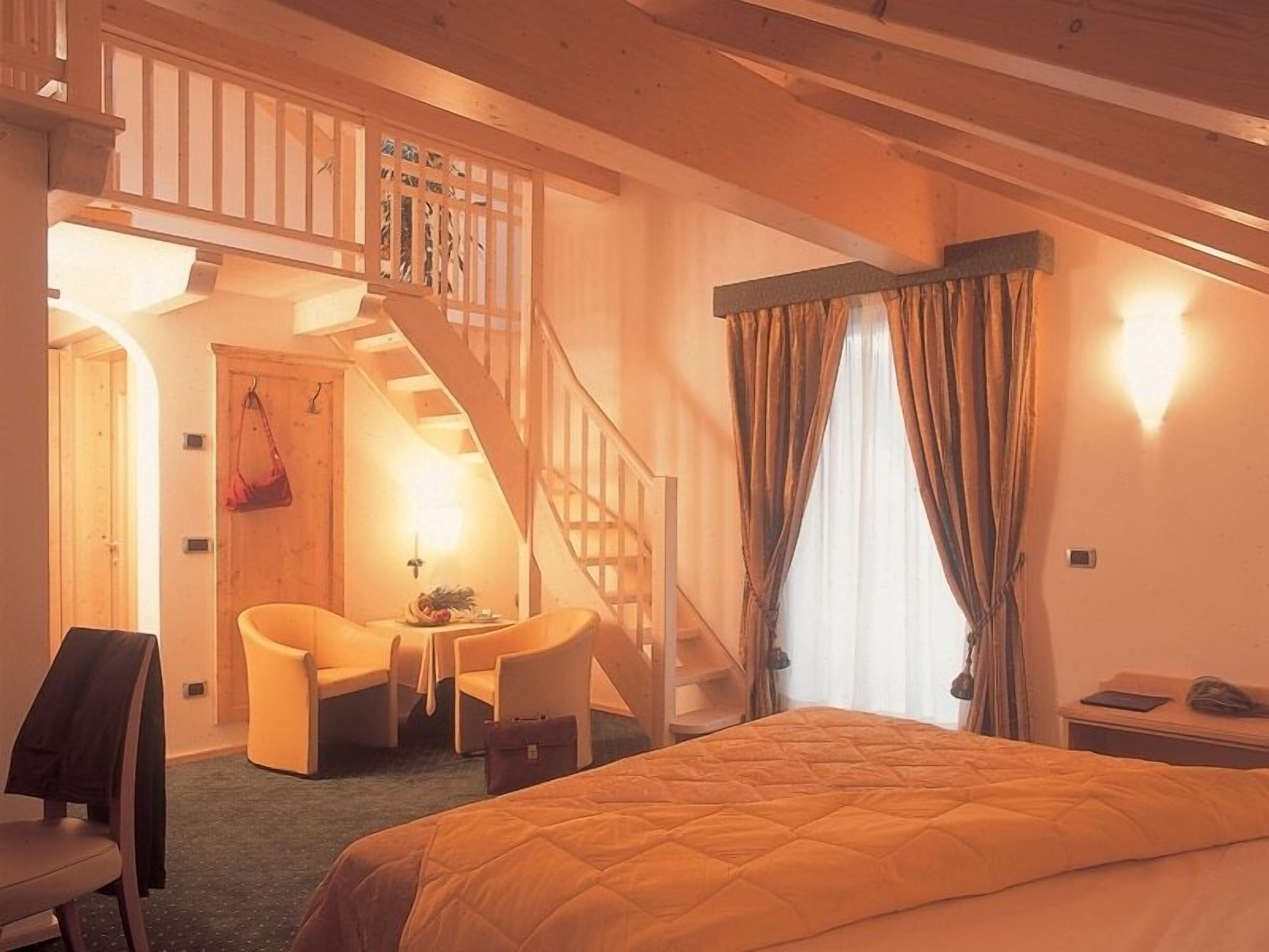 A cozy hotel room with a bed, a desk, a chair, and a staircase leading to an upper level.