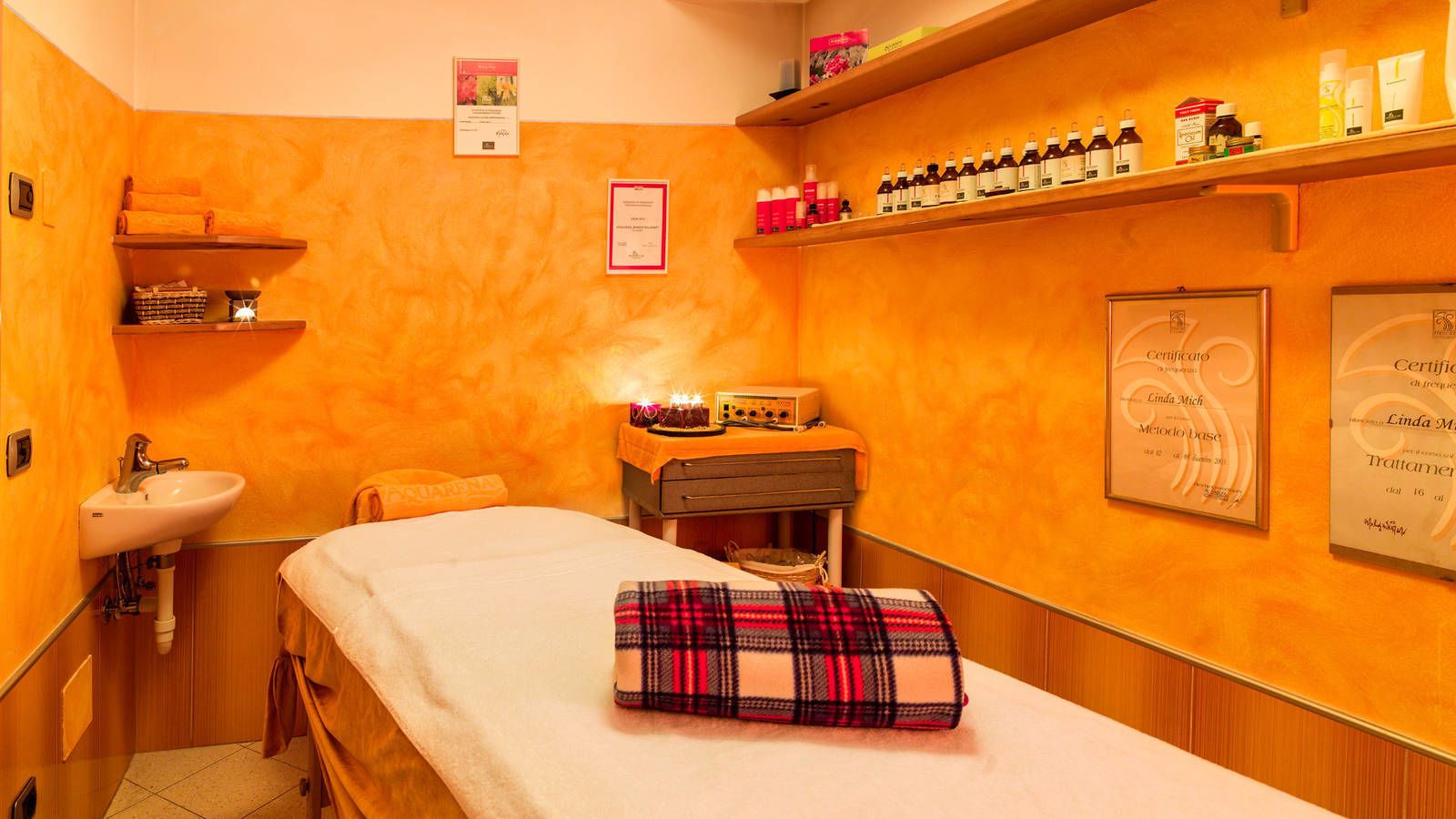 Ein Wellnessraum mit einem Bett, einem Waschbecken, Regalen mit Toilettenartikeln und Zertifikaten an der Wand.