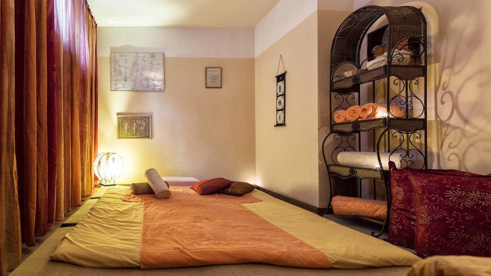 Un dormitorio con cama, mesita de noche, lámpara, reloj de pared y repisa decorativa.