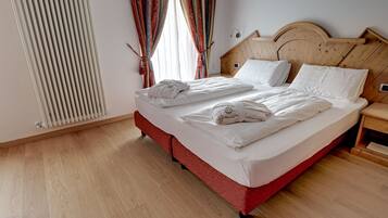 Cama doble con sábanas y toallas blancas, cabecera de madera y mesita de noche con lámpara.