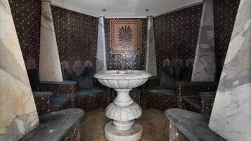 Relax in a serene bathroom with a central fountain, flanked by columns, and a mosaic-patterned wall.