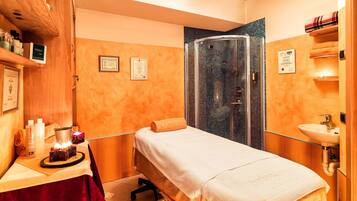Una stanza spa con lettino da massaggio, zona doccia e lavandino.