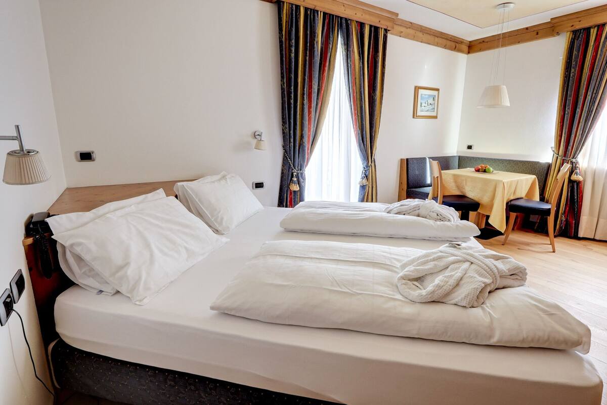 Una habitación de hotel con una cama grande, una mesita con sillas y una ventana con cortinas.