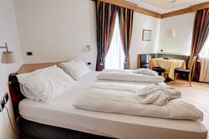 Una habitación de hotel con una cama grande, una mesita con sillas y una ventana con cortinas.