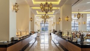 Un hall d’hôtel spacieux et bien éclairé, avec un long comptoir de réception, de nombreux lustres et une vue sur l’extérieur grâce à de grandes fenêtres.