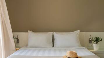 Un lit bien fait, avec du linge de lit blanc et un chapeau de paille posé sur le lit.