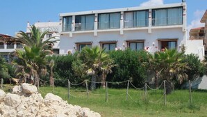 Un hotel de dos pisos con balcones, rodeado de palmeras y un área cercada.
