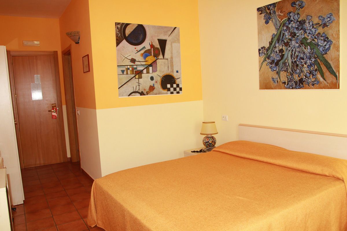 Camera d'albergo con un letto, una porta, un muro con arte astratta e un comodino con una lampada.