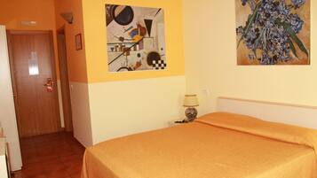 Camera d'albergo con un letto, una porta, un muro con arte astratta e un comodino con una lampada.