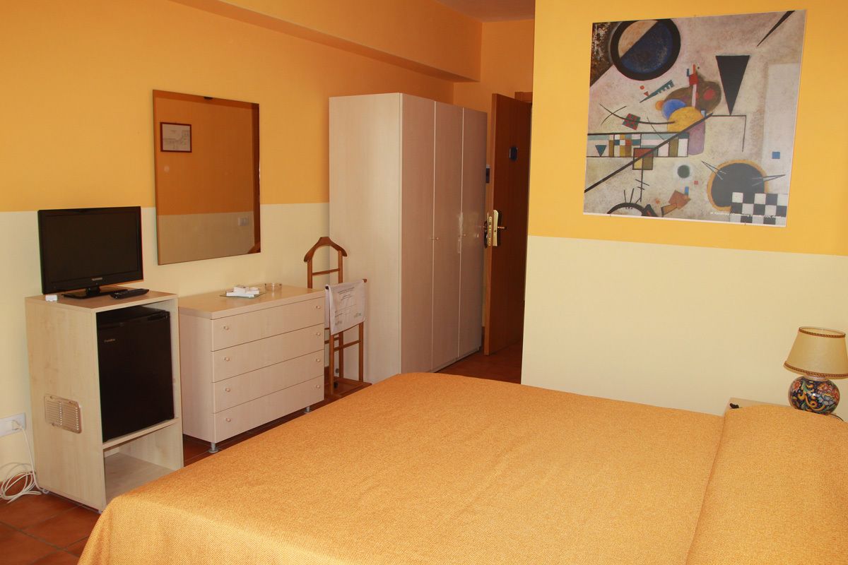 A hotel room with a bed, a television, a dresser, a wardrobe, and a painting on the wall.