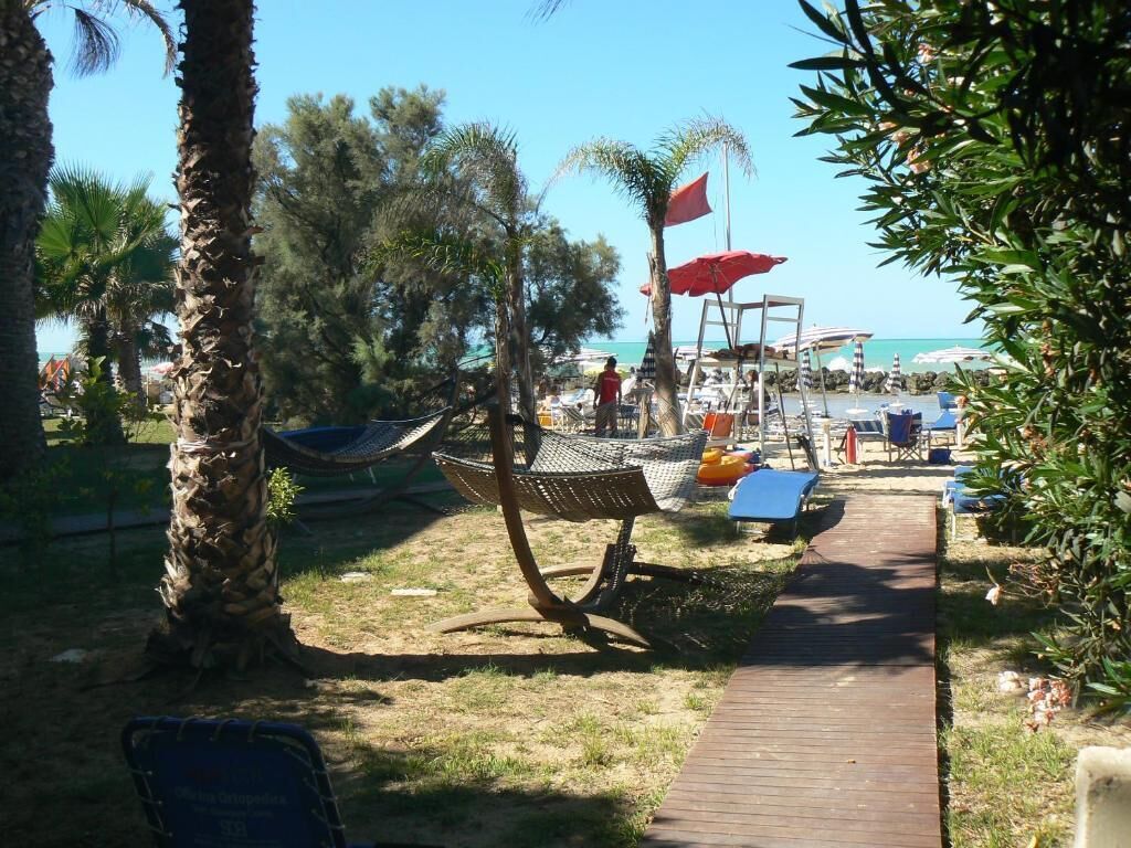 Un área junto a la playa con una hamaca, un camino de madera y sillas de playa.