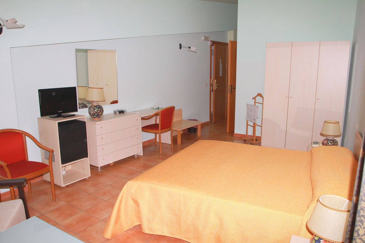 Un dormitorio con cama, escritorio, silla, televisor, cómoda y armario.