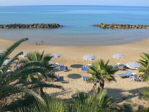 A beach with umbrellas and lounge chairs, palm trees, and a calm sea. - Al Gabbiano (Vittoria)