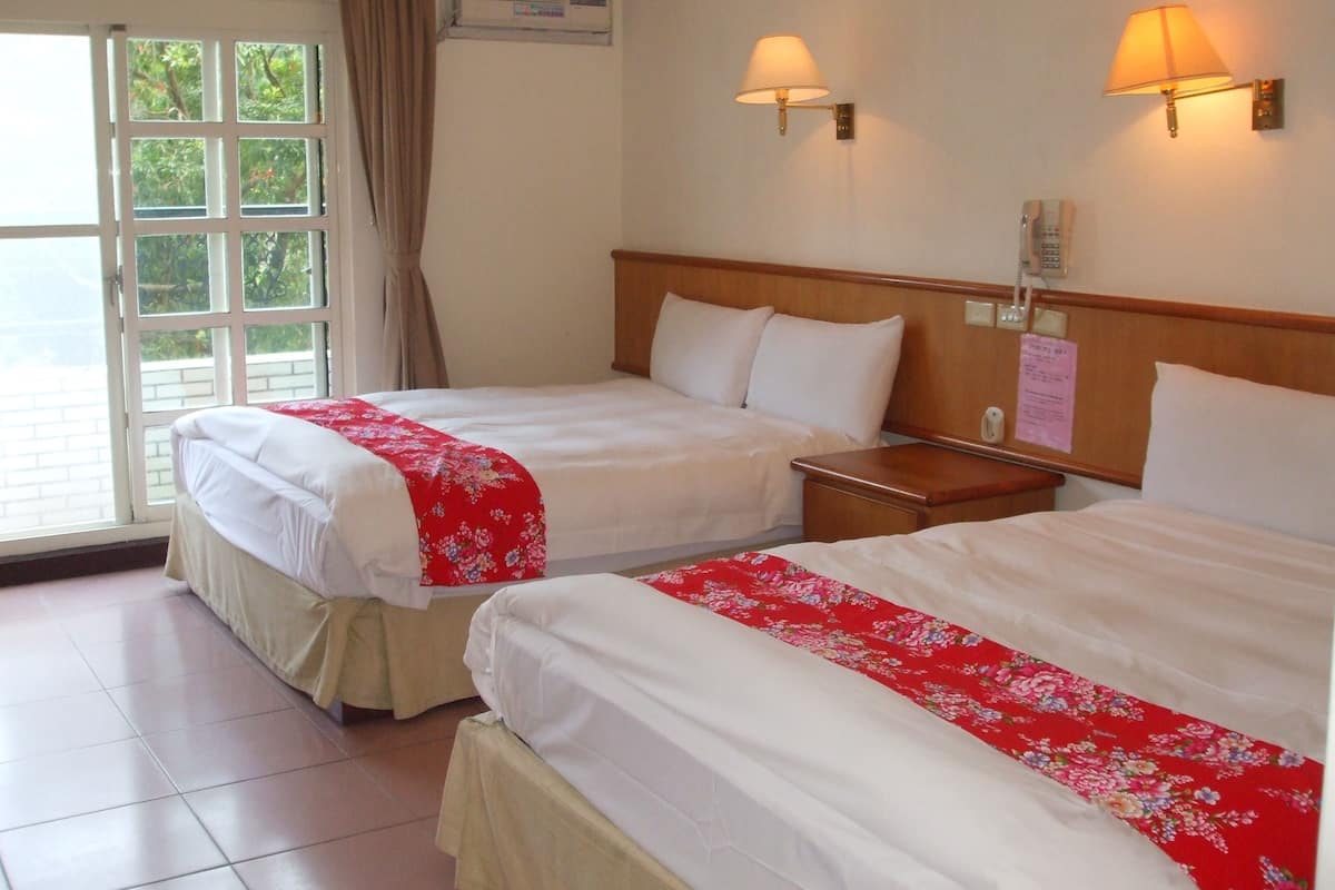 A hotel room with two beds, a window with curtains, a wall-mounted phone, and a thermostat.