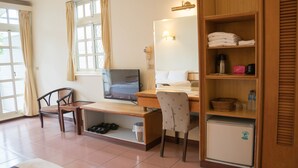 Hotellihuone, jossa on sänky, työpöytä tietokoneella, tuoli, pieni jääkaappi sekä hylly, jossa on pyyhkeitä ja hygieniatarvikkeita.