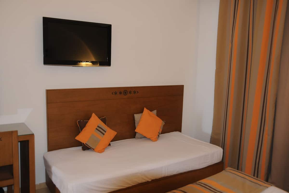 Uma cama bem arrumada com cabeceira de madeira, dois travesseiros e uma televisão de tela plana fixada na parede acima.