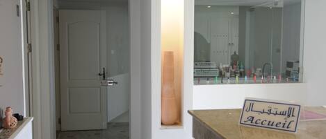 A hotel reception area with a marble counter, a sign reading "Accueil," and a view of the bathroom through a glass partition.