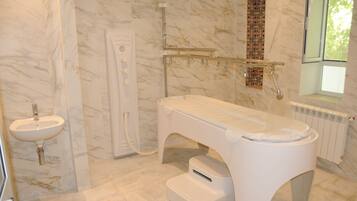 A bathroom with a marble floor, a white sink, a glass shower enclosure, and a window with a view of trees.