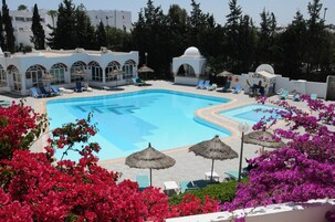 Una piscina con sillas de descanso y sombrillas, rodeada de flores y árboles.