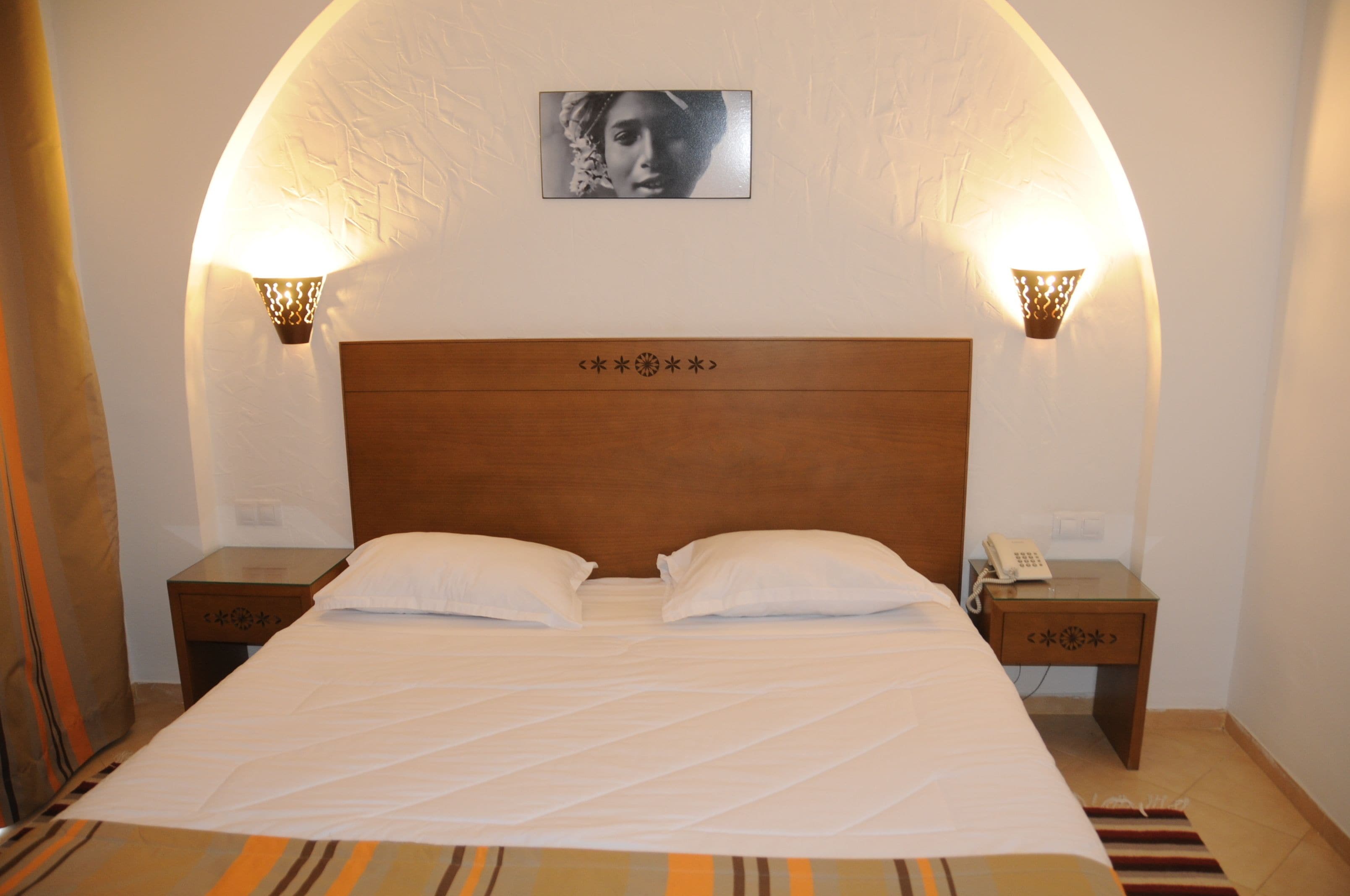 Una habitación de hotel con una cama grande, dos mesitas de noche y lámparas fijadas a la pared.