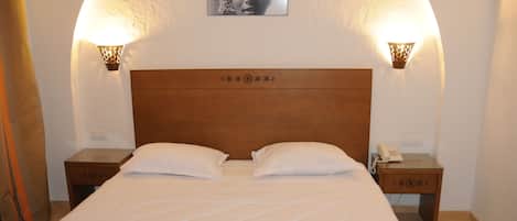 A hotel room with a large bed, two bedside tables, and wall-mounted lamps.