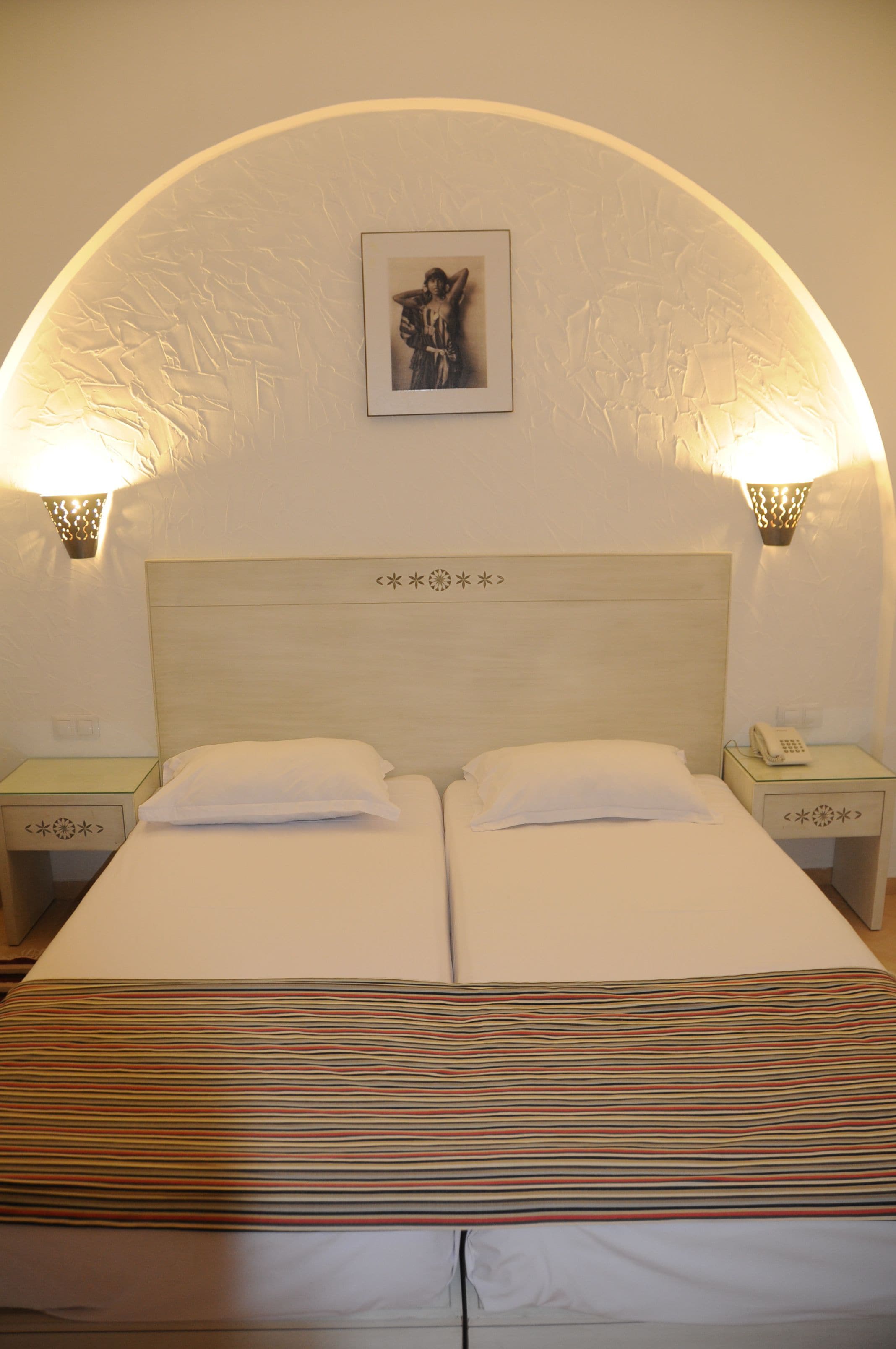 A double bed with white linens, two bedside tables with lamps, and a framed picture on the wall.