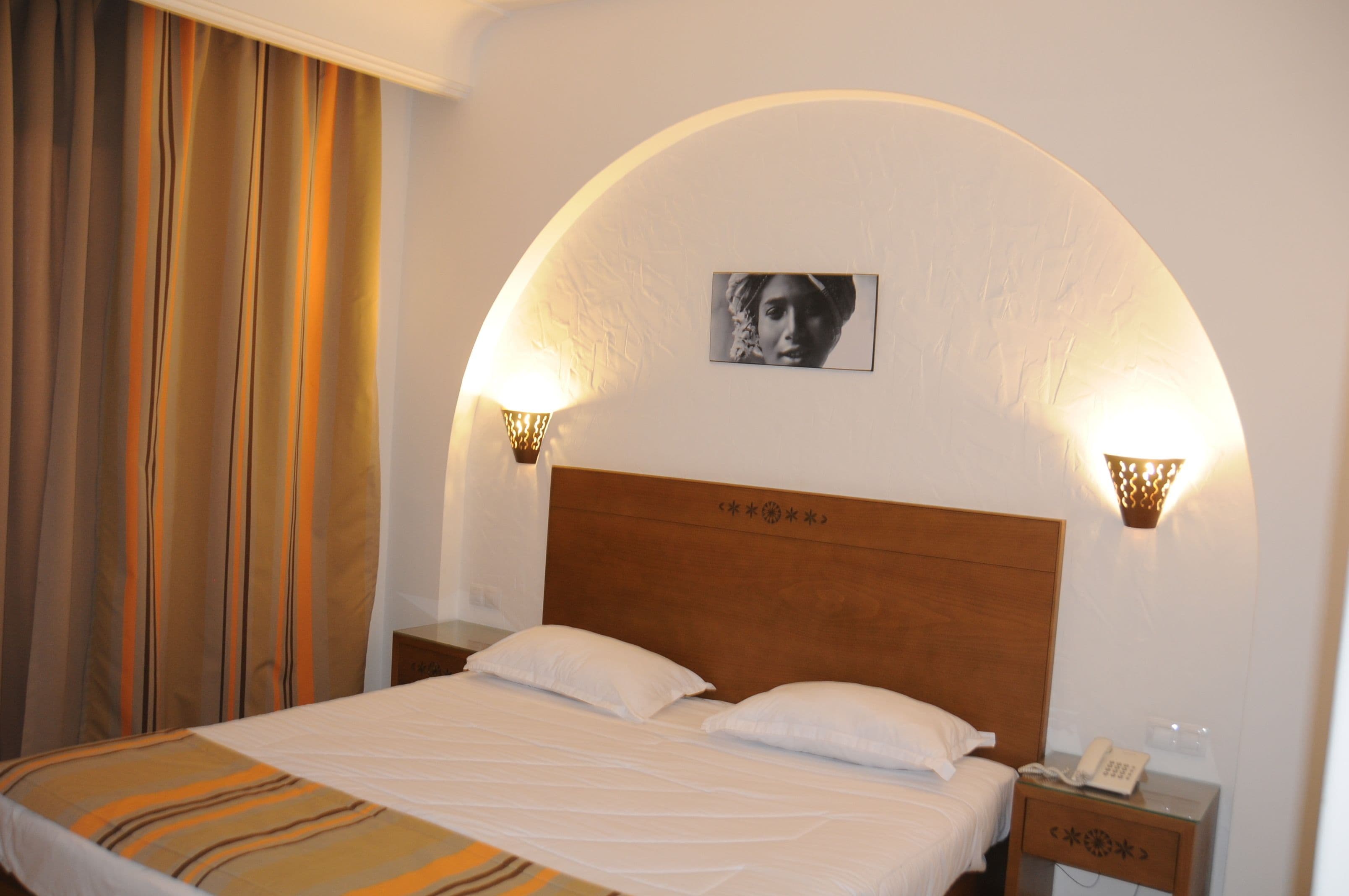 Een hotelkamer met een bed, twee bedlampen, een nachtkastje met een telefoon en een foto aan de muur.