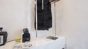 Ein weißer Tresen mit einem schwarzen Kleidungsstück an einem Gestell, einer Kaffeemaschine, einem Tablet und einer Tablett mit Tassen und einer kleinen Schokoladenschachtel.
