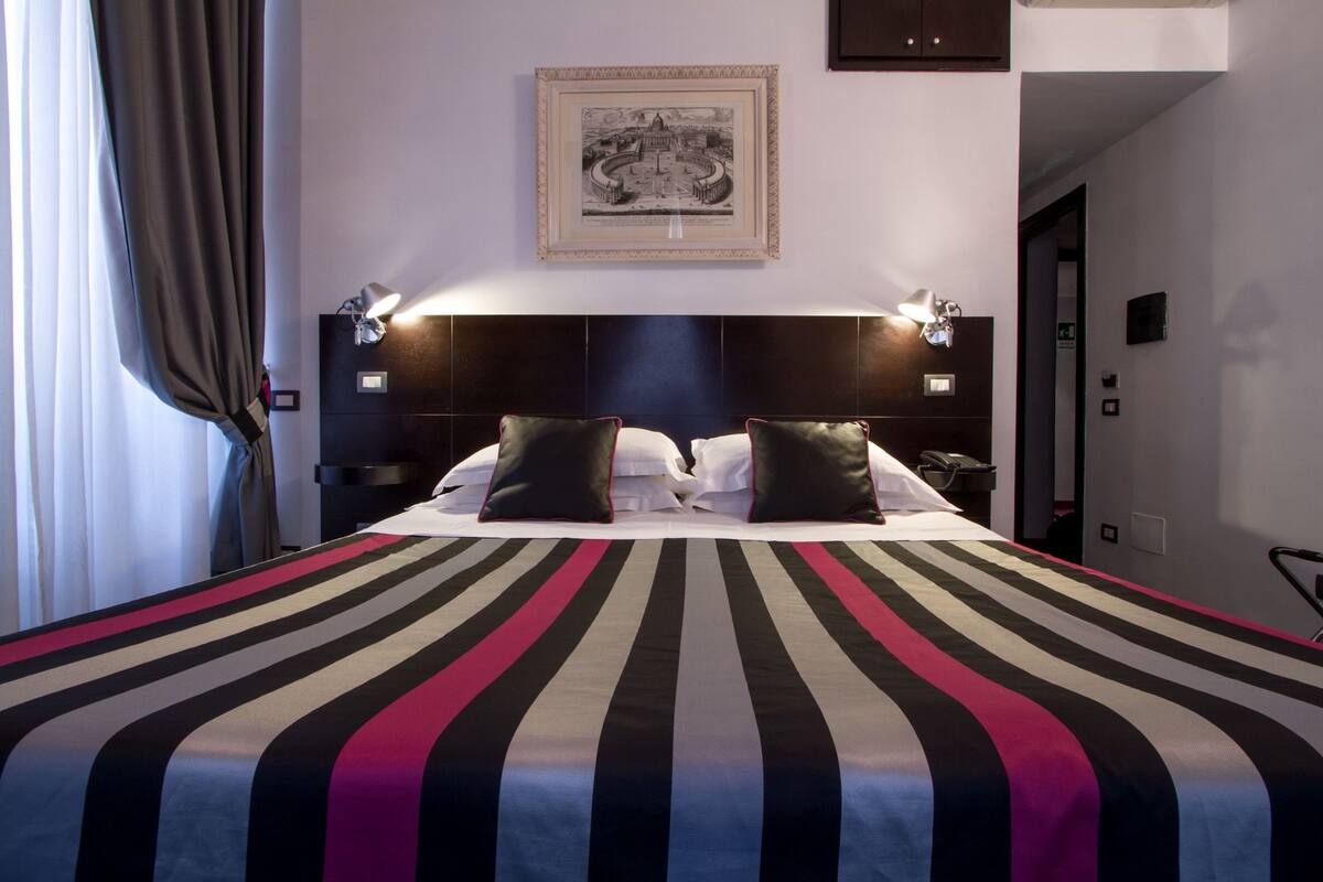 A hotel room with a large bed, a framed picture on the wall, and a nightstand with a lamp.