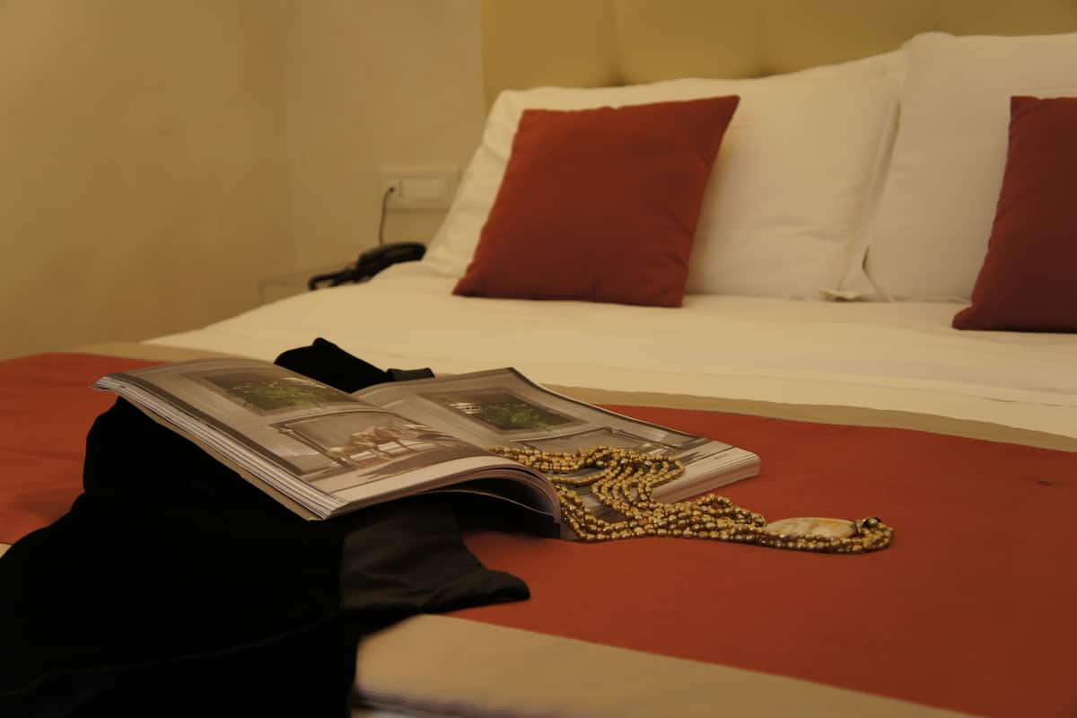 A bed with red bedding, a book, and a chain necklace on it.