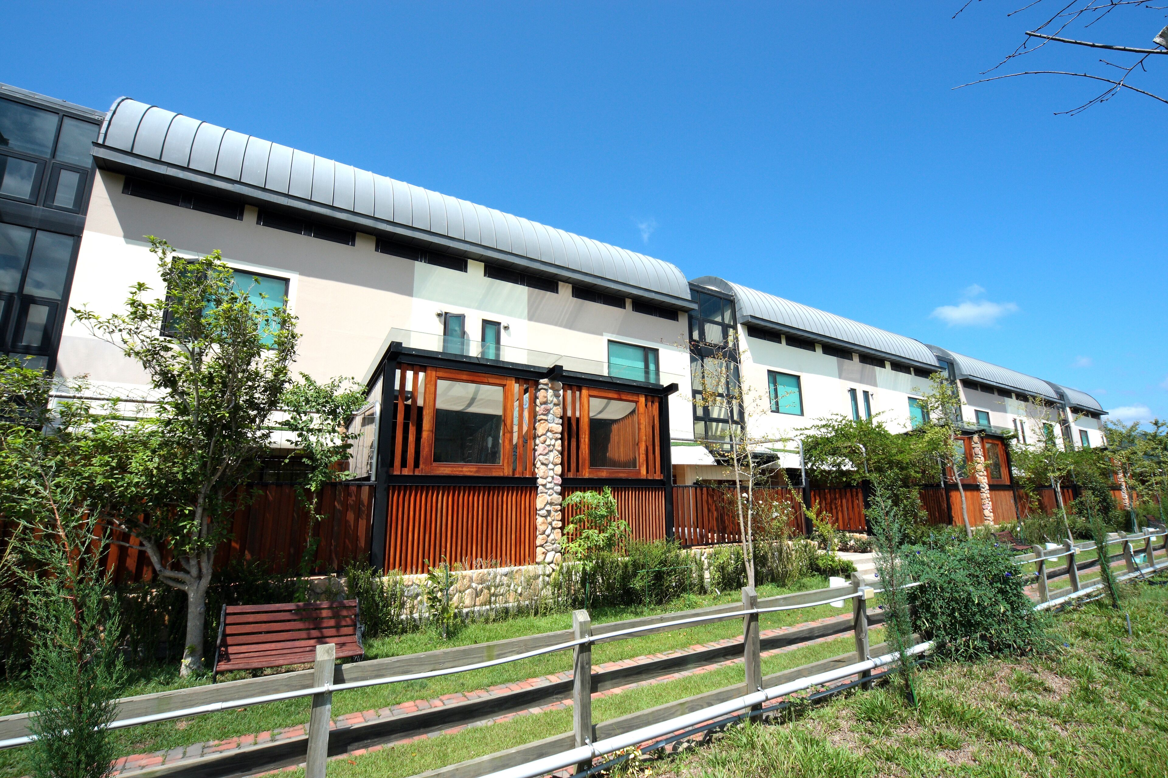 A modern building with a flat roof, large windows, and a wooden fence.