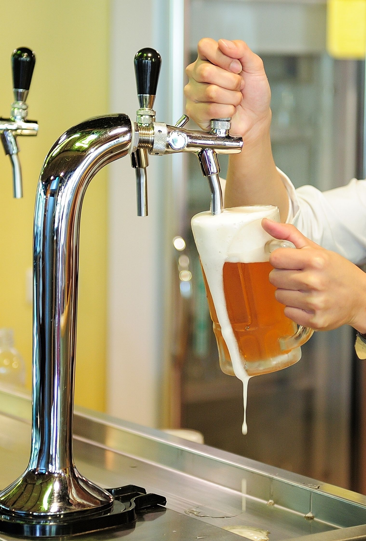 A hand holding a glass of beer being poured from a tap.